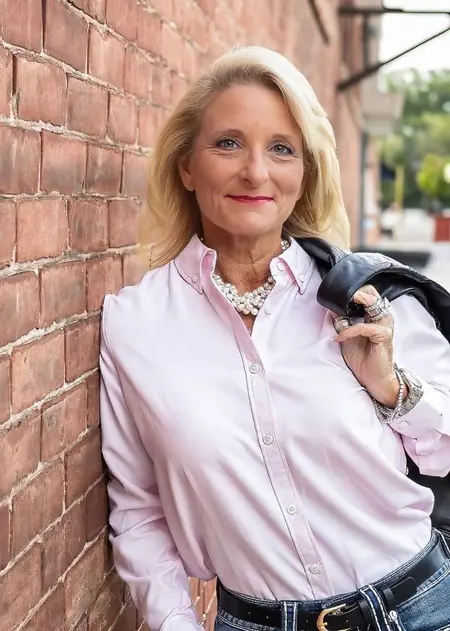 She didn’t choose the brick wall behind her by accident.

Years earlier, this alley had been a shortcut she took every morning on her way to school where her ideas were dismissed and her voice was softened to make others comfortable. She learned quickly that leadership isn’t given—it’s claimed. So she began preparing in quiet ways: studying after long days, asking hard questions, and saying no when it would have been easier to agree.

The jacket over her shoulder tells part of the story. It’s the weight of responsibility she learned to carry without letting it bend her posture. When a crisis hit the company she later led, people looked to her not because she was the loudest in the room, but because she was steady. She listened when others panicked. She decided when others hesitated.

There were moments of real fear—standing alone in boardrooms, making calls that could cost millions, choosing integrity when shortcuts were tempting. Courage, she discovered, wasn’t dramatic. It was calm. It showed up early and stayed late. It took accountability when things went wrong and shared credit when things went right.

Success didn’t arrive as applause. It arrived as trust. Teams grew stronger under her leadership. People stayed, learned, and rose. She built something sustainable, not flashy—something that lasted.

Now, when she pauses against this wall, she’s not resting. She’s reflecting. The faint smile isn’t for the camera—it’s for the woman she used to be, the one who kept walking even when the path was narrow.

Strength brought her here. Leadership keeps her moving forward.